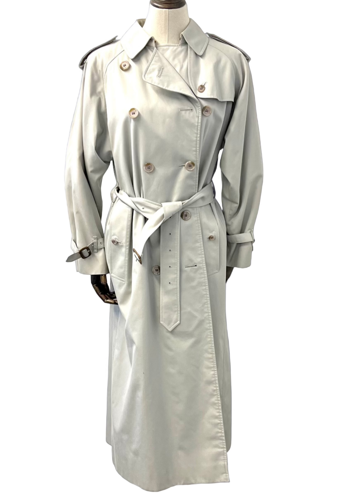 A light grey trench coat with leather buckles on cuff and belt, displayed on a mannequin.